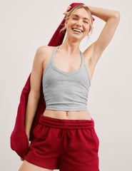 model wearing a gray v-neck cropped tank with a high racerback and red shorts with a red jacket over her shoulder on a light background.