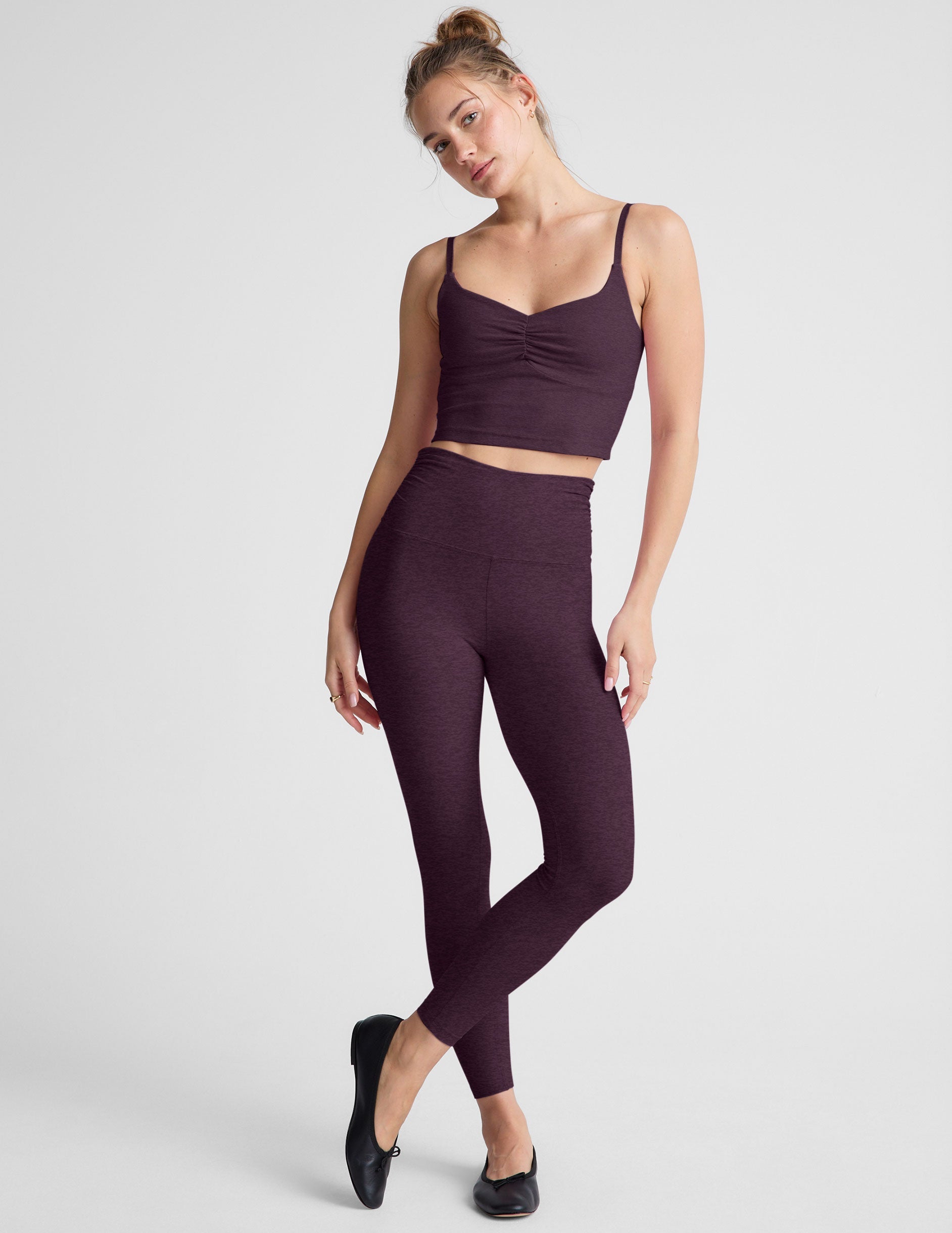 model wearing a purple cropped tank top with shirring at center front and purple high-waisted midi length leggings against a plain background.