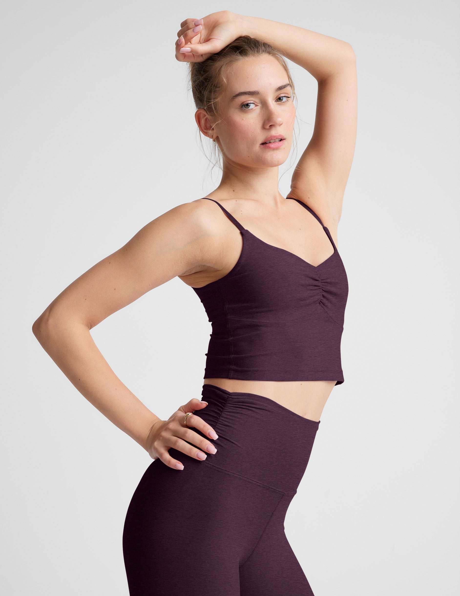 model wearing a purple cropped tank top with shirring at center front and purple high-waisted midi length leggings against a plain background.