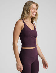 model is wearing a purple v-neck tank top with criss-cross strap back detail and purple high-waisted midi length leggings on a plain background.