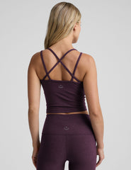 model is wearing a purple v-neck tank top with criss-cross strap back detail and purple high-waisted midi length leggings on a plain background.