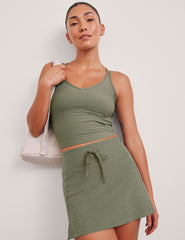 green waist length tank top with a v-neck and overlapping strap detail on back.