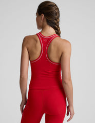 woman wearing a red waist length racerback tank top with white piping on a plain background.