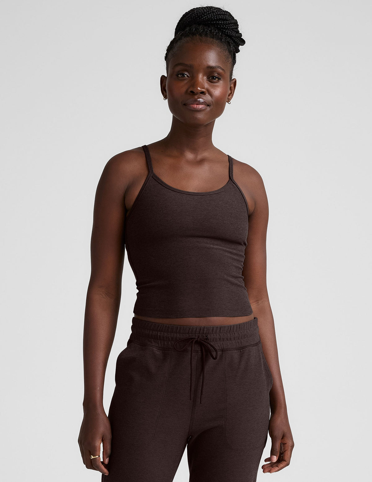 Woman wearing a brown midway length tank top with adjustable straps and brown jogger pants against a plain background.