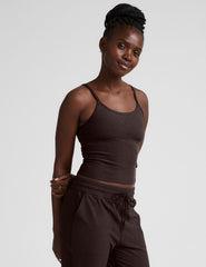 Woman wearing a brown midway length tank top with adjustable straps and brown jogger pants against a plain background.