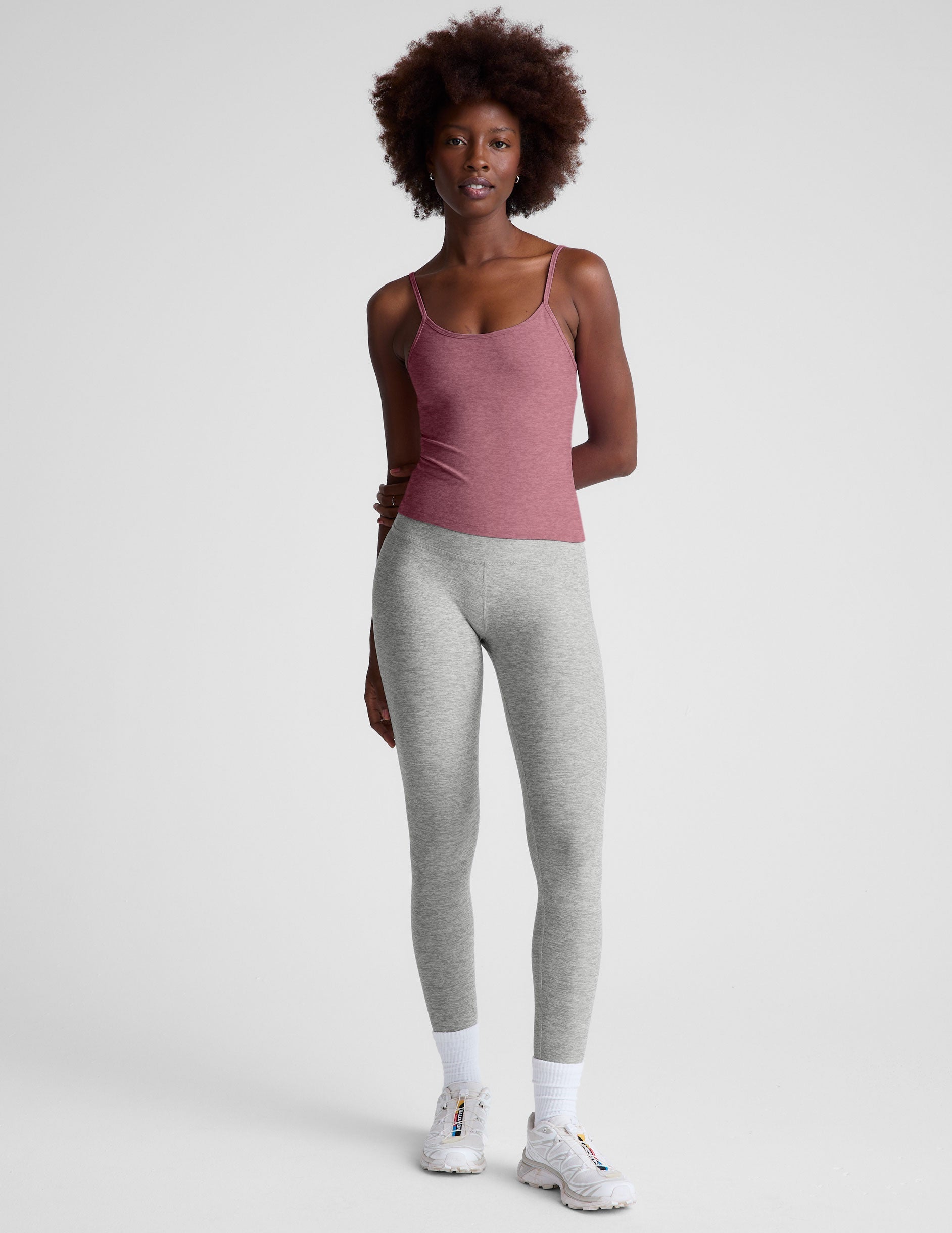 model is wearing a pink midway length tank top with adjustable straps and gray leggings against a plain background.