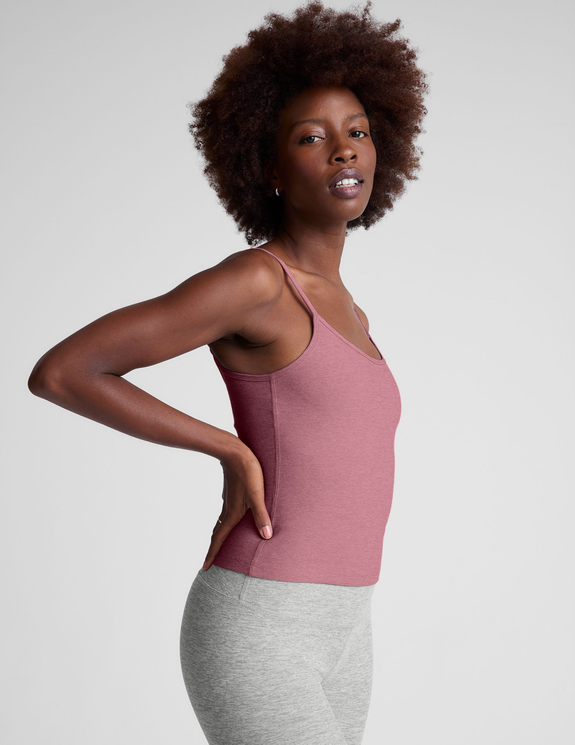 model is wearing a pink midway length tank top with adjustable straps and gray leggings against a plain background.