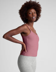 model is wearing a pink midway length tank top with adjustable straps and gray leggings against a plain background.