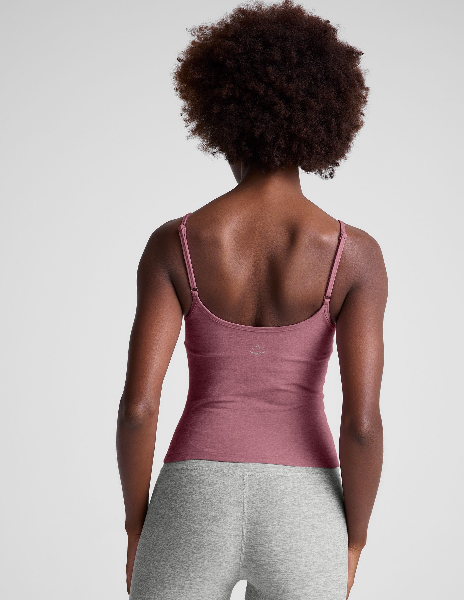 model is wearing a pink midway length tank top with adjustable straps and gray leggings against a plain background.