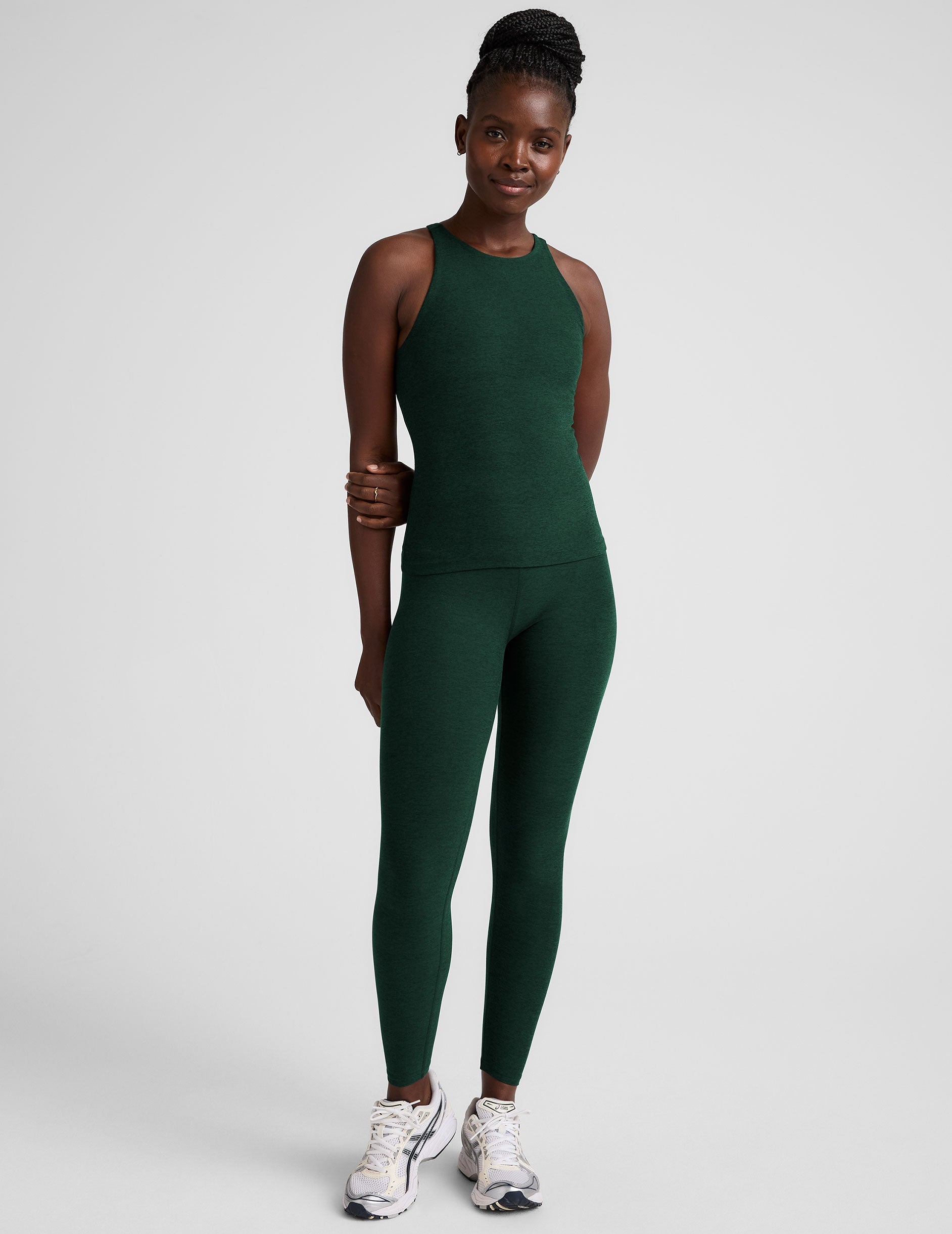model is wearing a green high neck full length racerback tank top and leggings against a plain background.