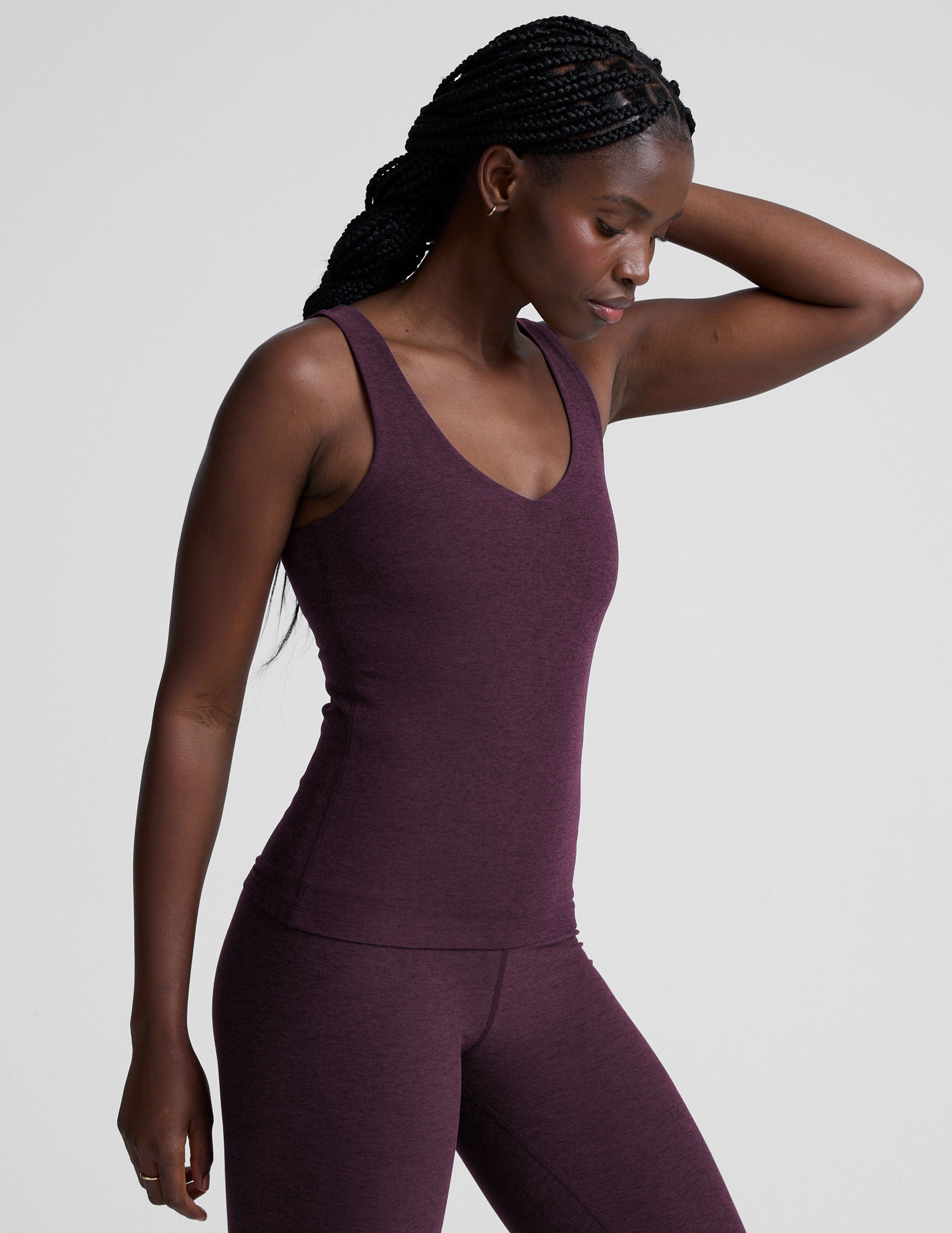 woman wearing a purple tank top and leggings on a light gray background.