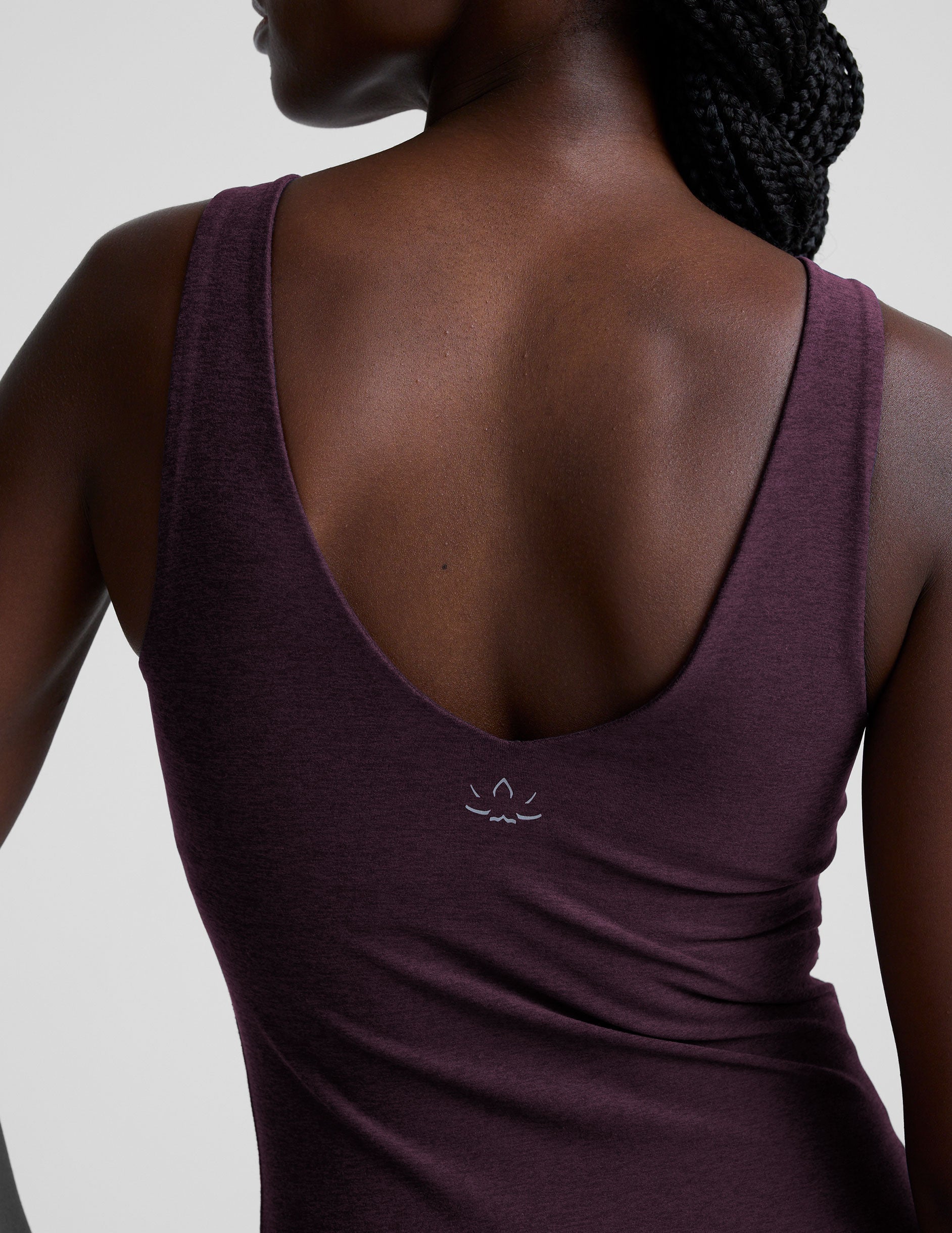 woman wearing a purple tank top and leggings on a light gray background.