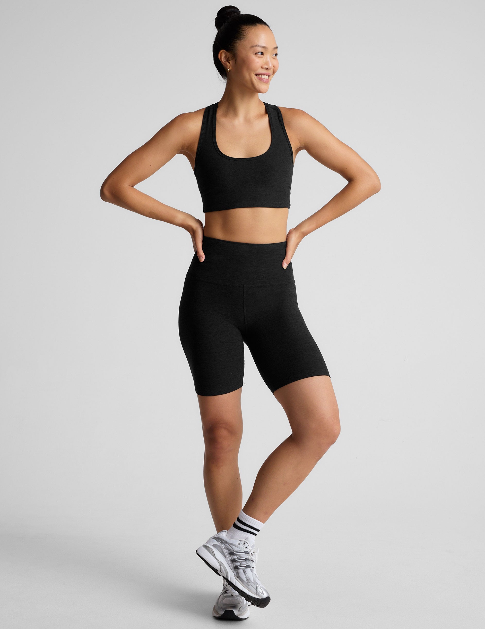 Woman wearing a black sports bra and biker shorts on a light gray background