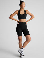 Woman wearing a black sports bra and biker shorts on a light gray background