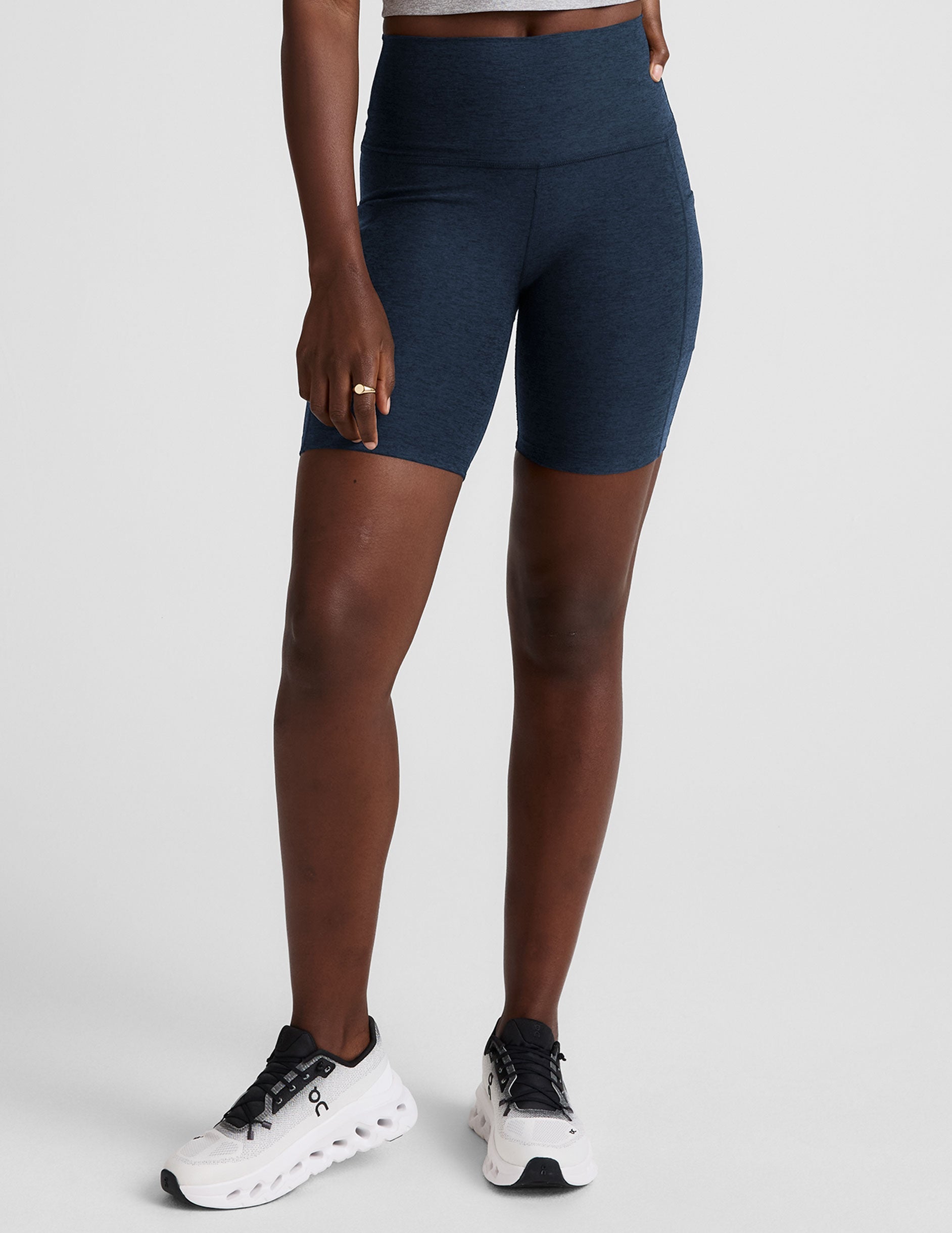 woman wearing navy blue biker shorts with pockets on a plain background.