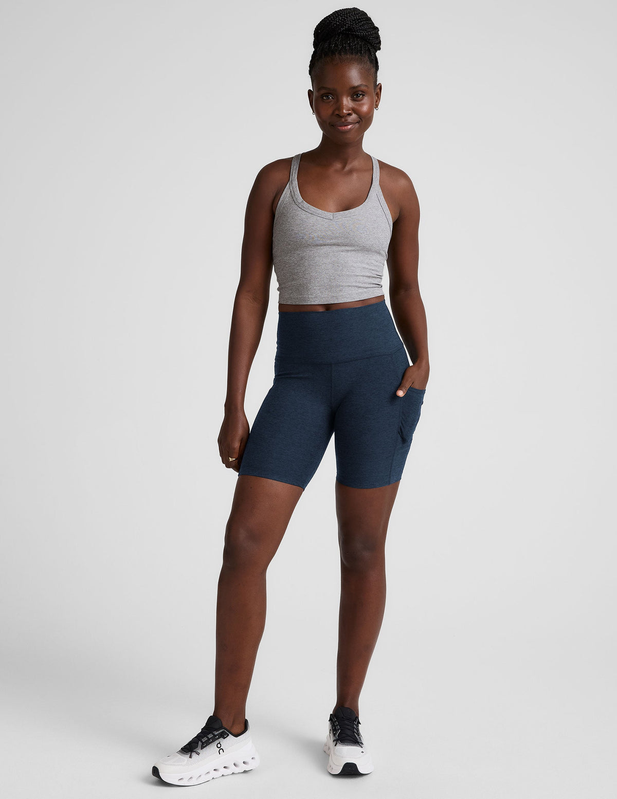 woman wearing a gray tank top and navy blue biker shorts with pockets on a plain background.