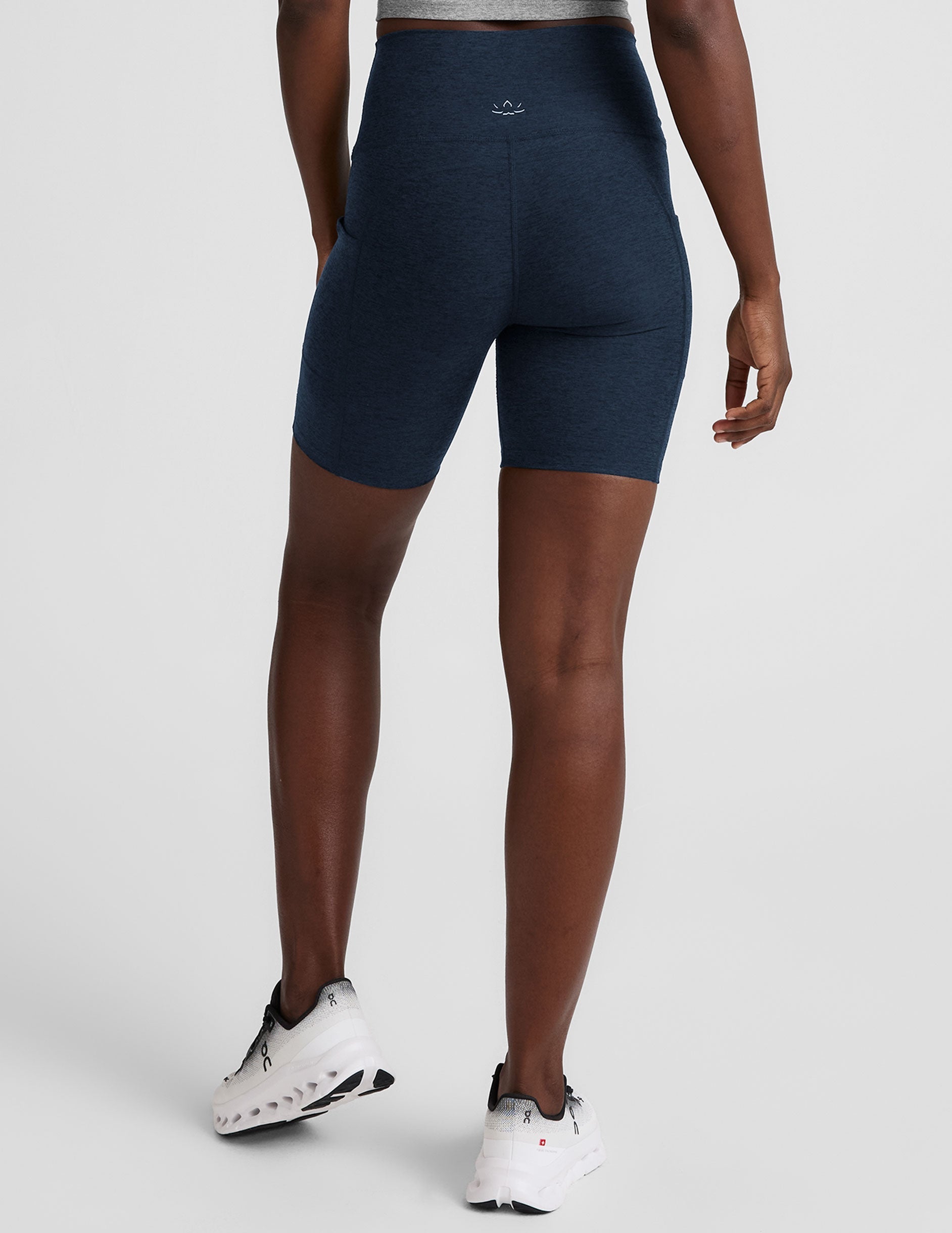 woman wearing navy blue biker shorts with pockets on a plain background.