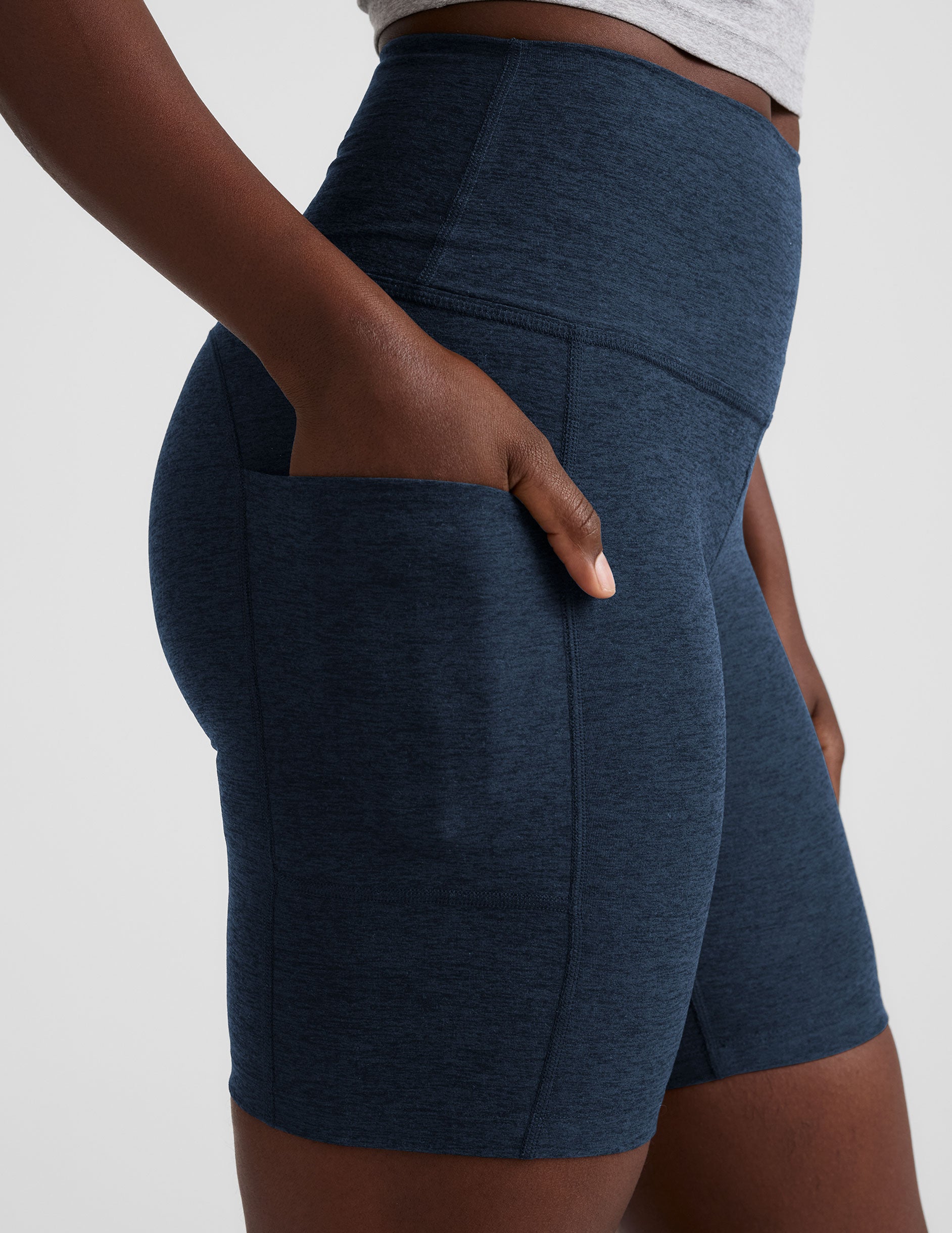 woman wearing navy blue biker shorts with pockets on a plain background.
