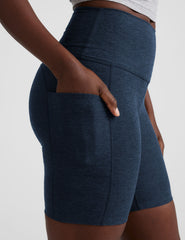 woman wearing navy blue biker shorts with pockets on a plain background.