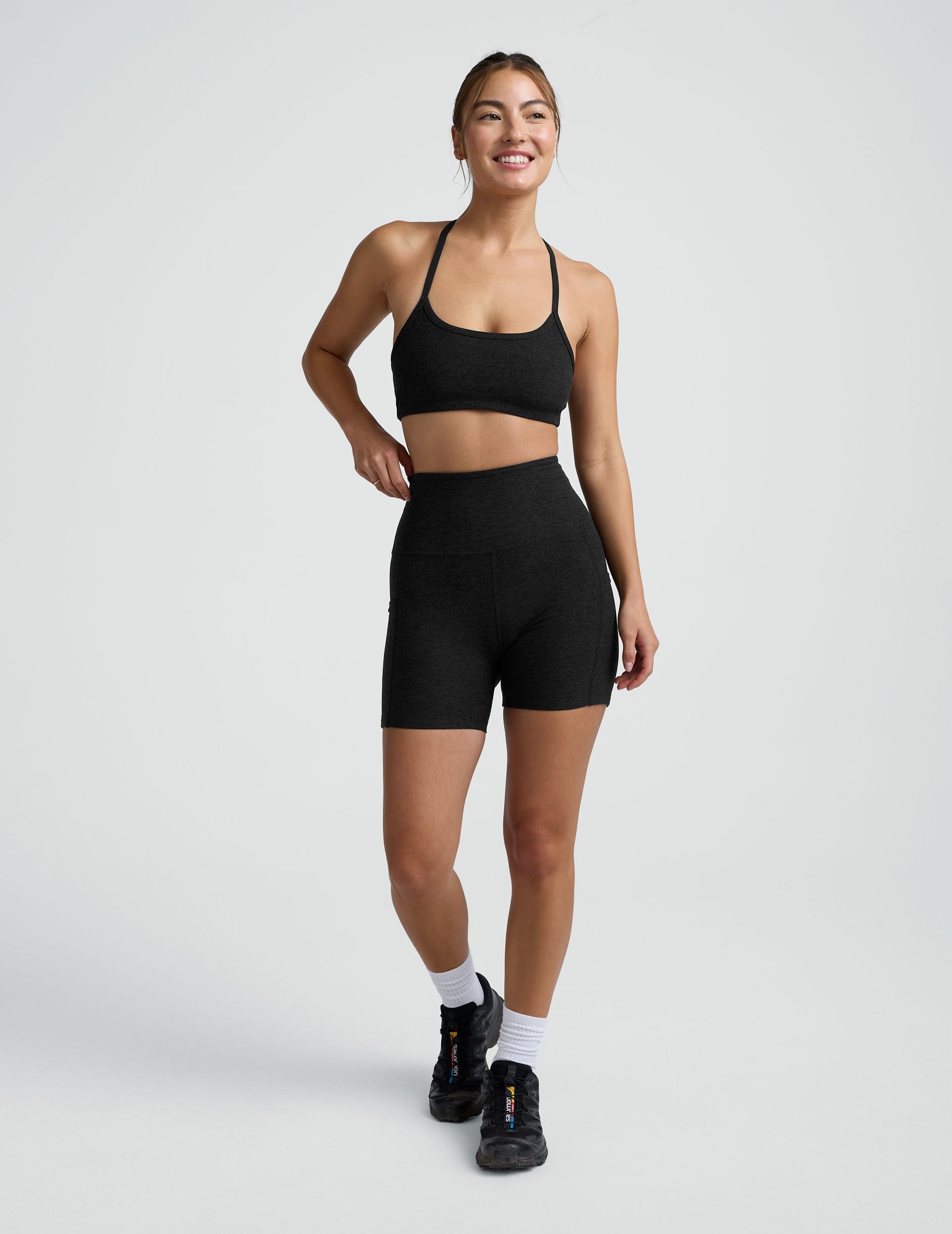 woman wearing a black sports bra and pocket biker shorts shorts on a plain background.