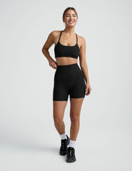 woman wearing a black sports bra and pocket biker shorts shorts on a plain background.