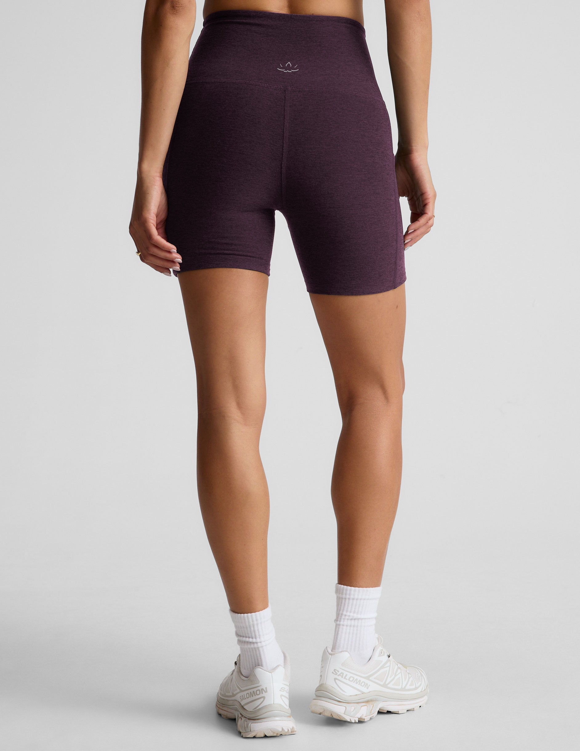 model is wearing a purple sports bra and purple 5" biker shorts with pockets against a plain background. 