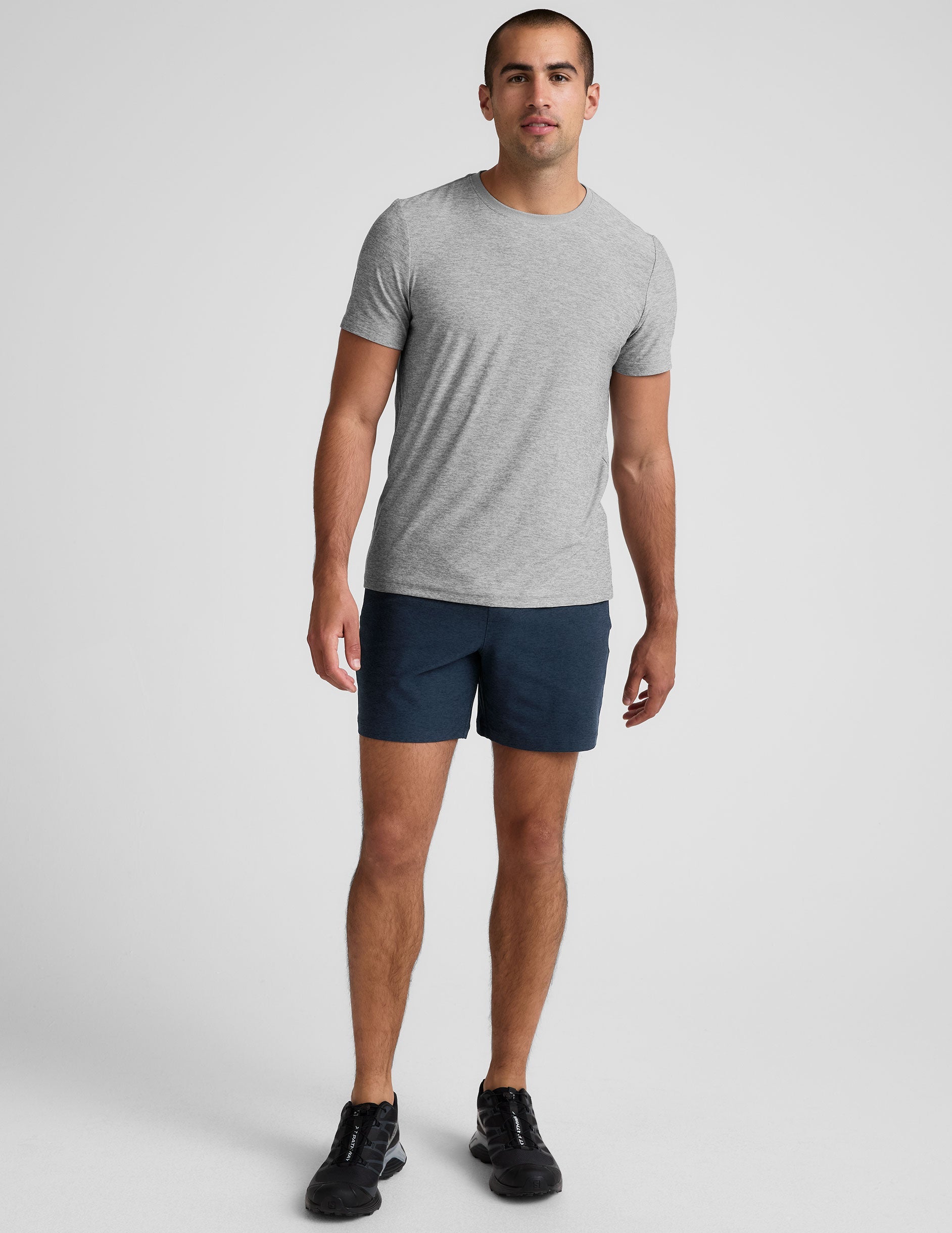 man wearing a grey t-shirt and navy blue shorts on a plain background.