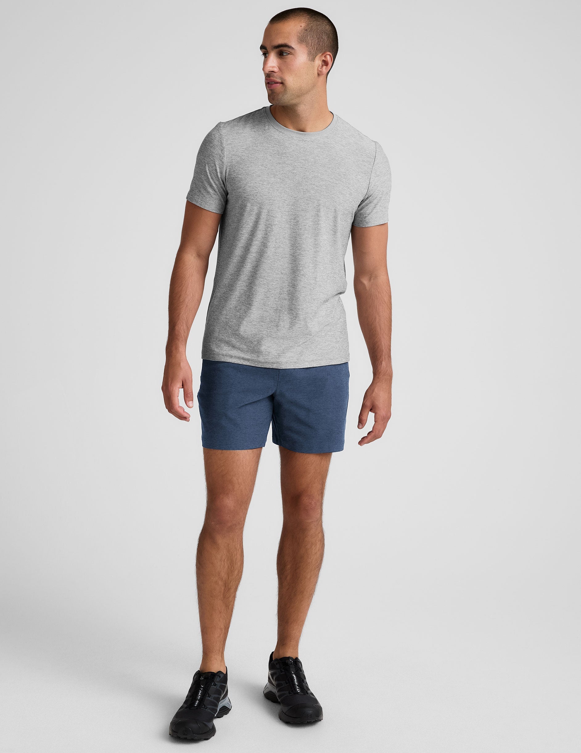 man wearing a grey t-shirt and blue shorts on a plain background.