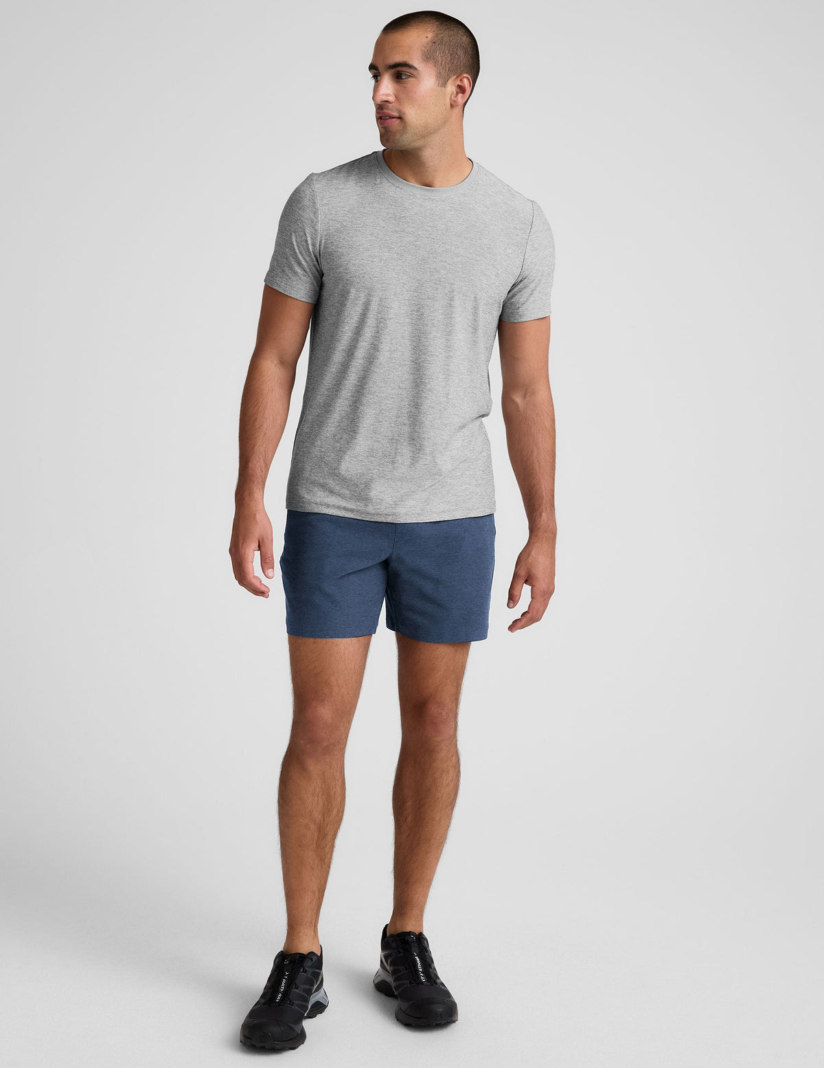 man wearing a grey t-shirt and blue shorts on a plain background.
