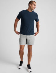 man wearing a navy t-shirt and gray shorts on a plain background.