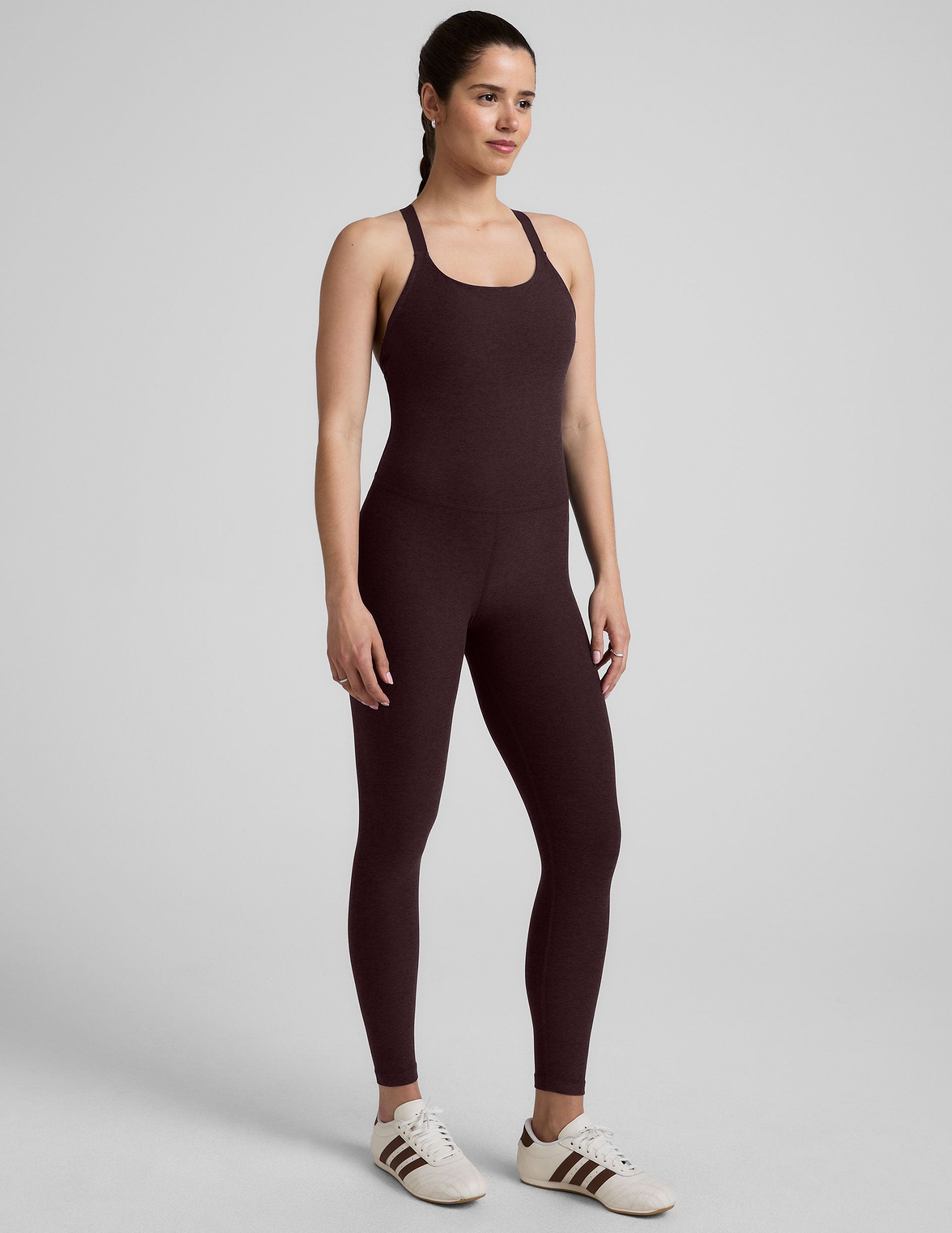 woman wearing a dark brown midi length jumpsuit on a plain background.