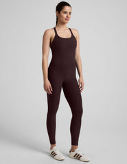 woman wearing a dark brown midi length jumpsuit on a plain background.