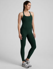 model wearing a green midi length tank jumpsuit with criss-cross back straps on a plain background.
