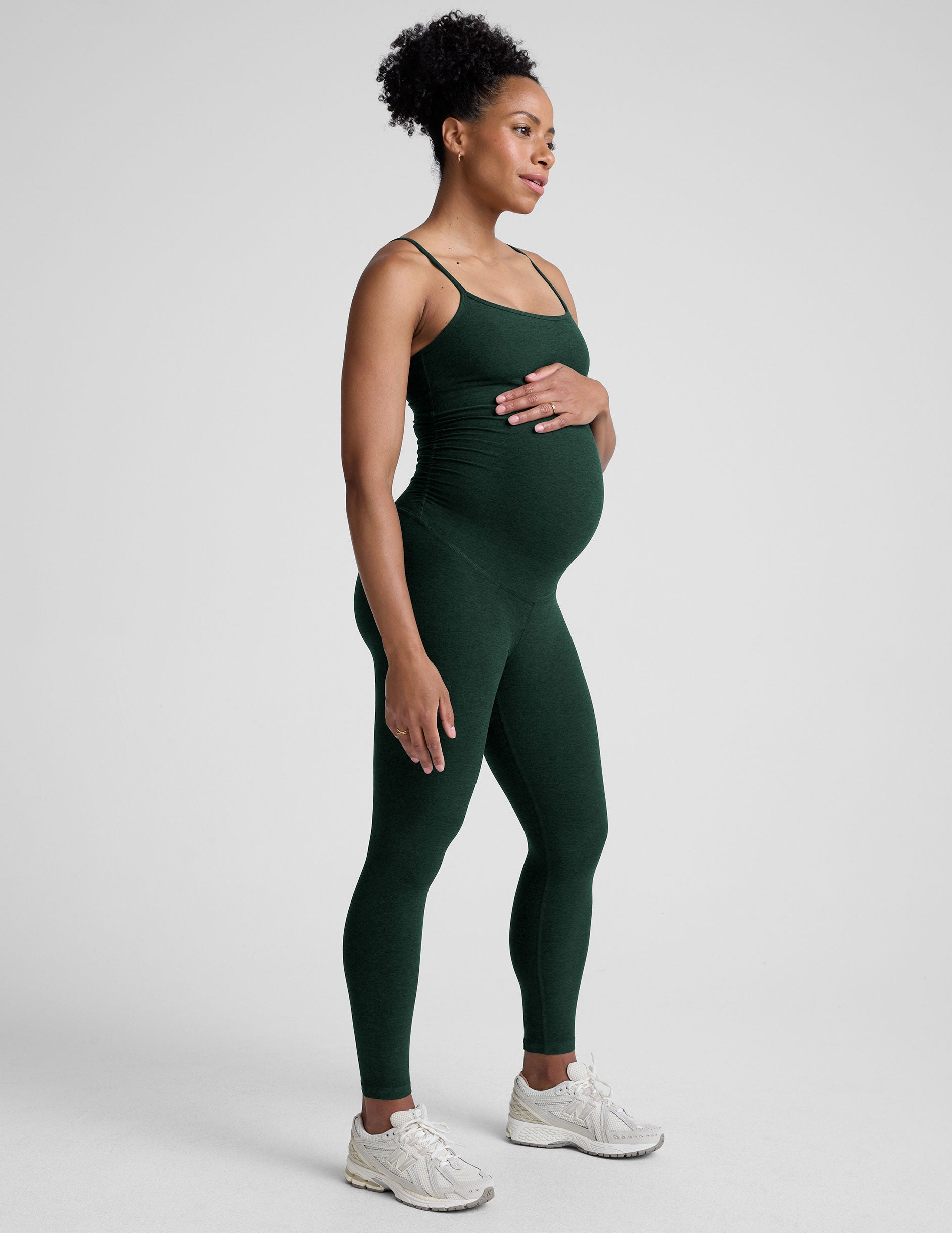 pregnant model wearing a green midi length maternity tank jumpsuit against a plain background.
