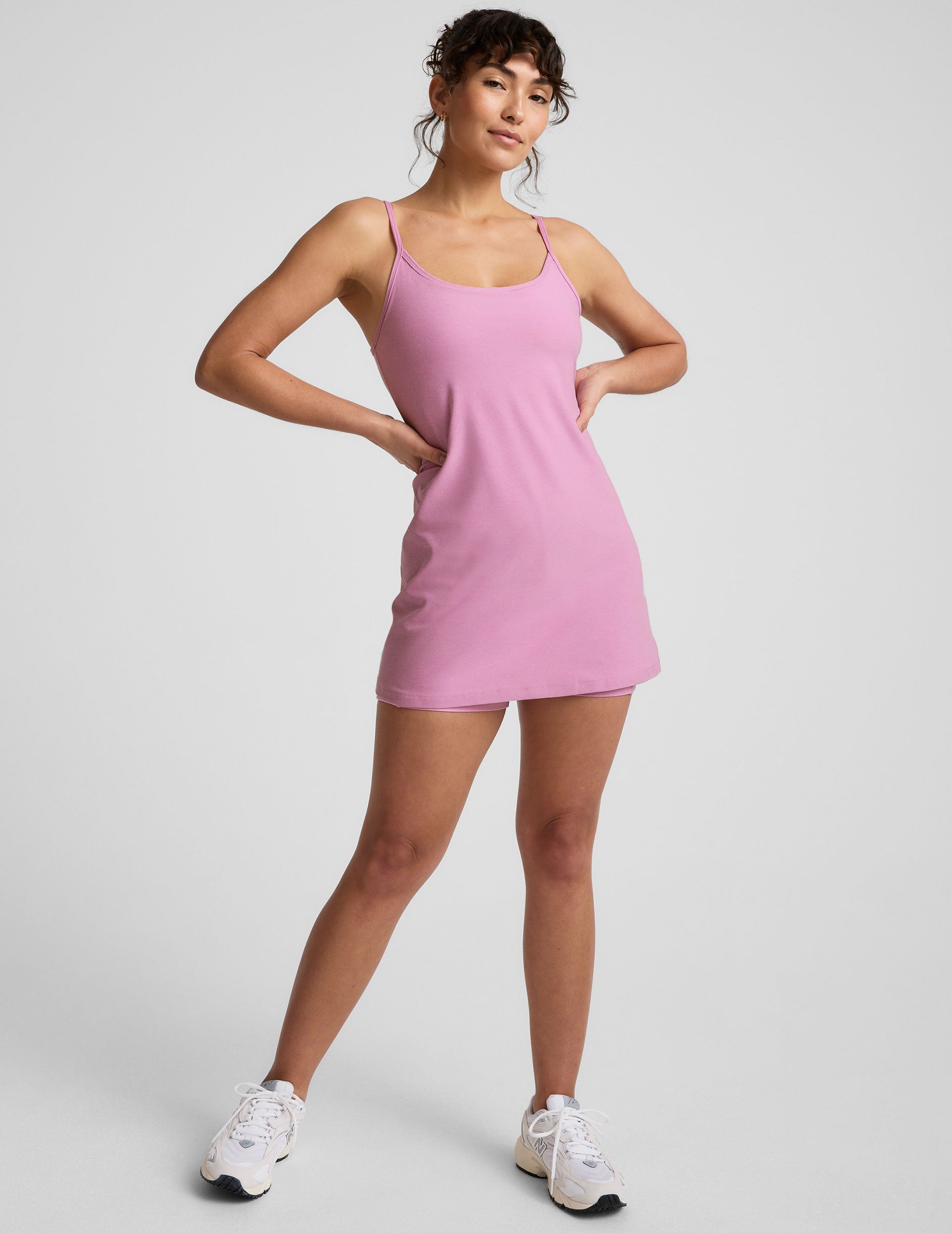model is wearing a pink mini length dress with slim adjustable straps and built-in shorts with pockets.