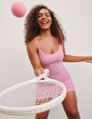 model is wearing a pink mini length dress with slim adjustable straps and built-in shorts with pockets.