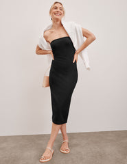 model is wearing a black midi length strapless dress with a back slit.