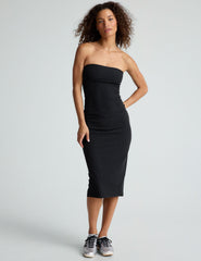 model is wearing a black midi length strapless dress with a back slit.