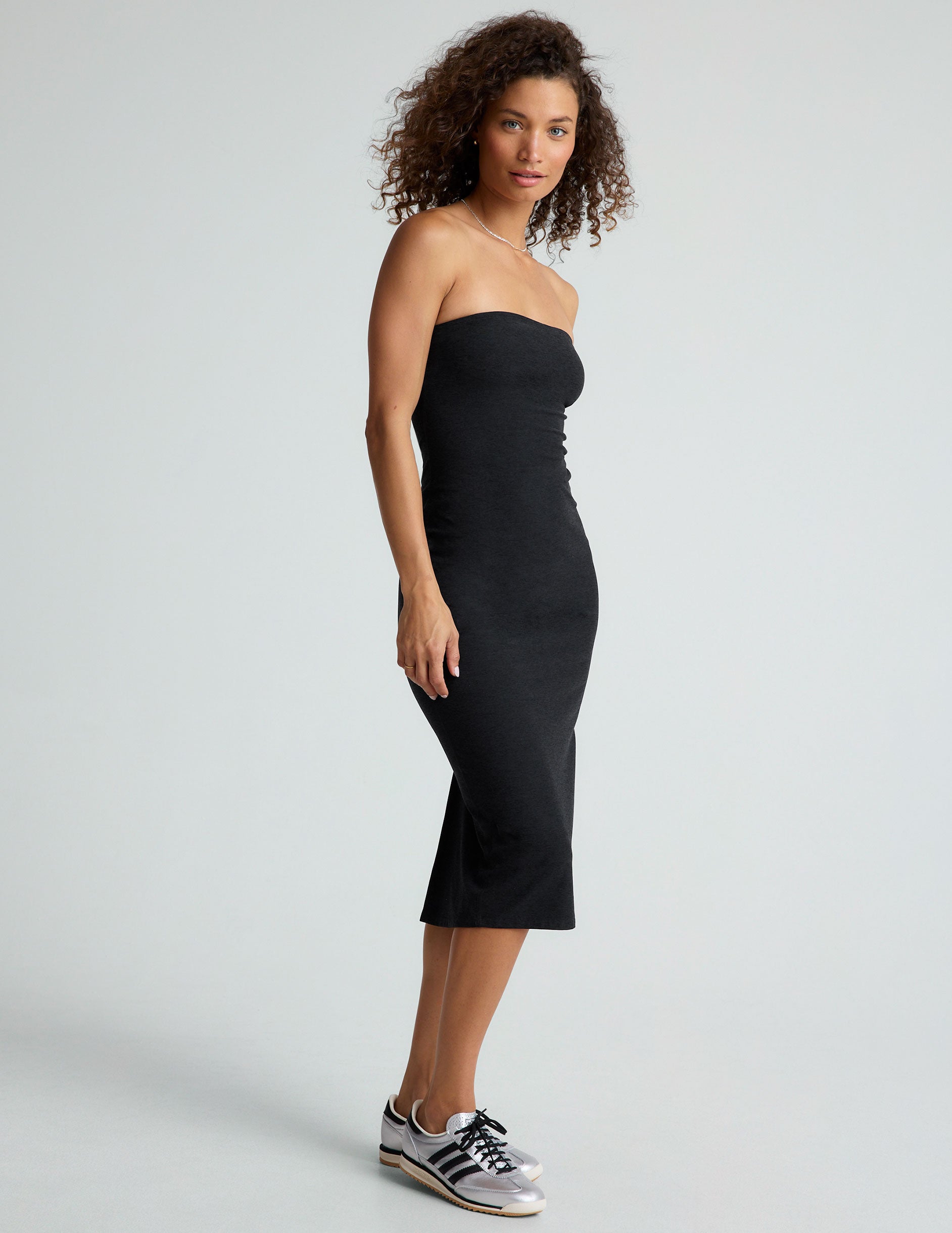 model is wearing a black midi length strapless dress with a back slit.