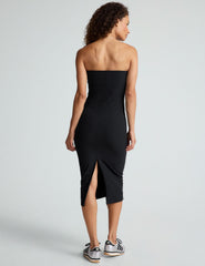 model is wearing a black midi length strapless dress with a back slit.