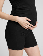 woman wearing a black maternity sleeveless jumpsuit on a plain background.