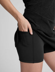 black mini length dress with a front V neckline​, back keyhole detail​, contrast binding at neckline and arm openings, and an Interior bodysuit with pockets​. 