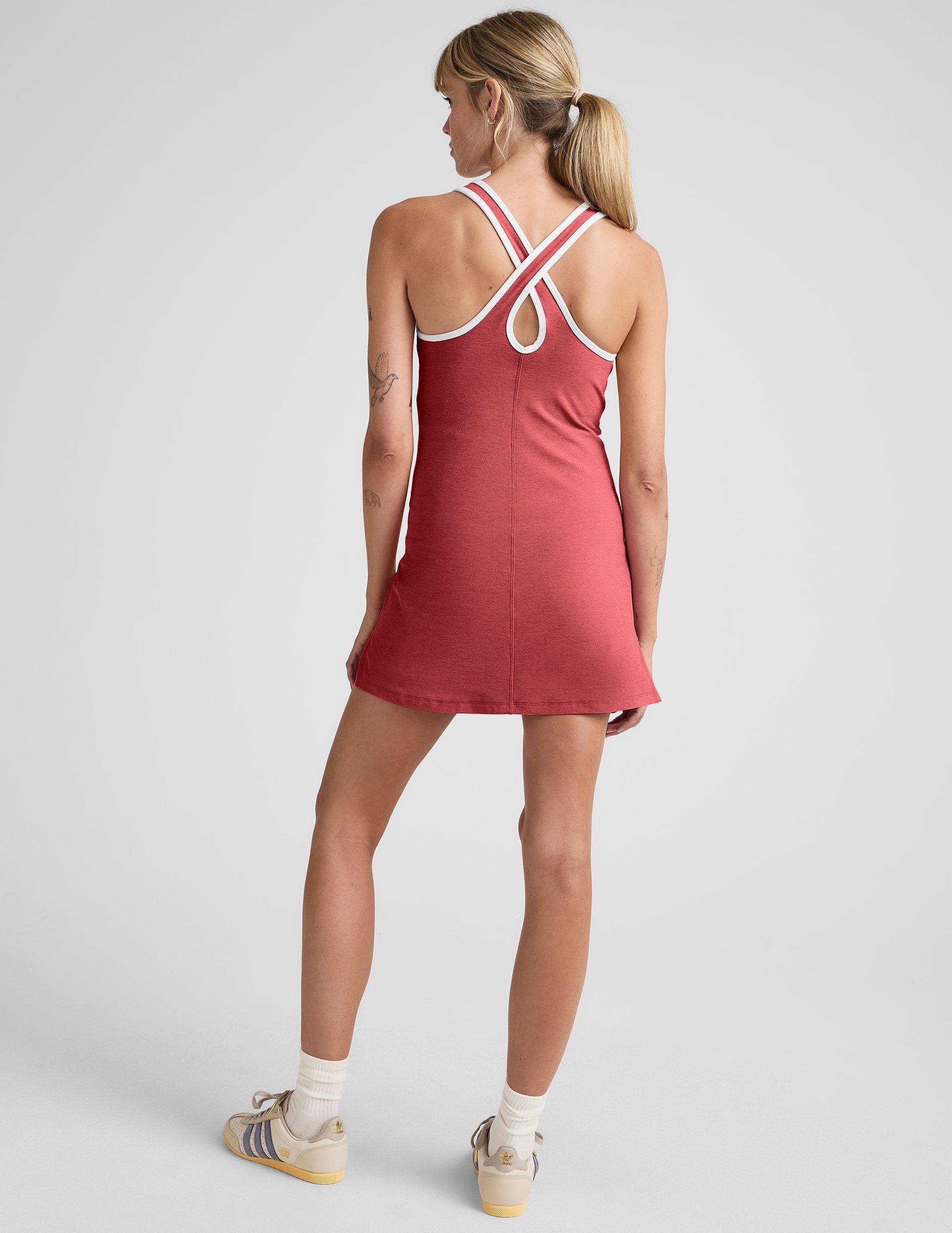model wearing a red mini athletic dress with white contrast trim and built in shorts on a plain background.