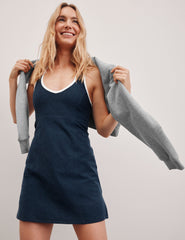 navy blue mini length dress with a front V neckline​, back keyhole detail​, contrast binding at neckline and arm openings, and an Interior bodysuit with pockets​. 