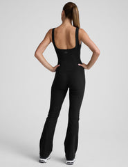 model wearing a black square neck and bootcut jumpsuit on a gray background.