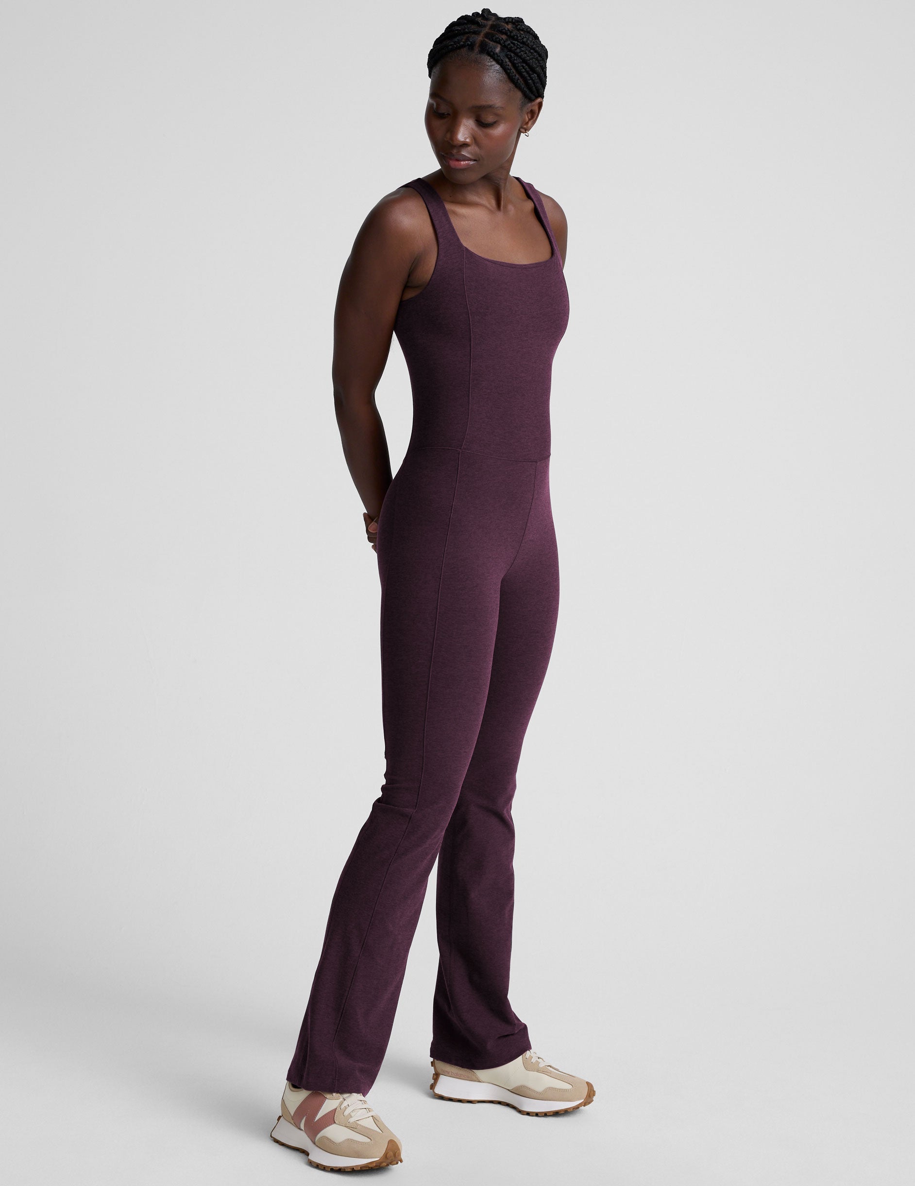 model wearing a purple square neck bootcut sleeveless jumpsuit on a plain background.