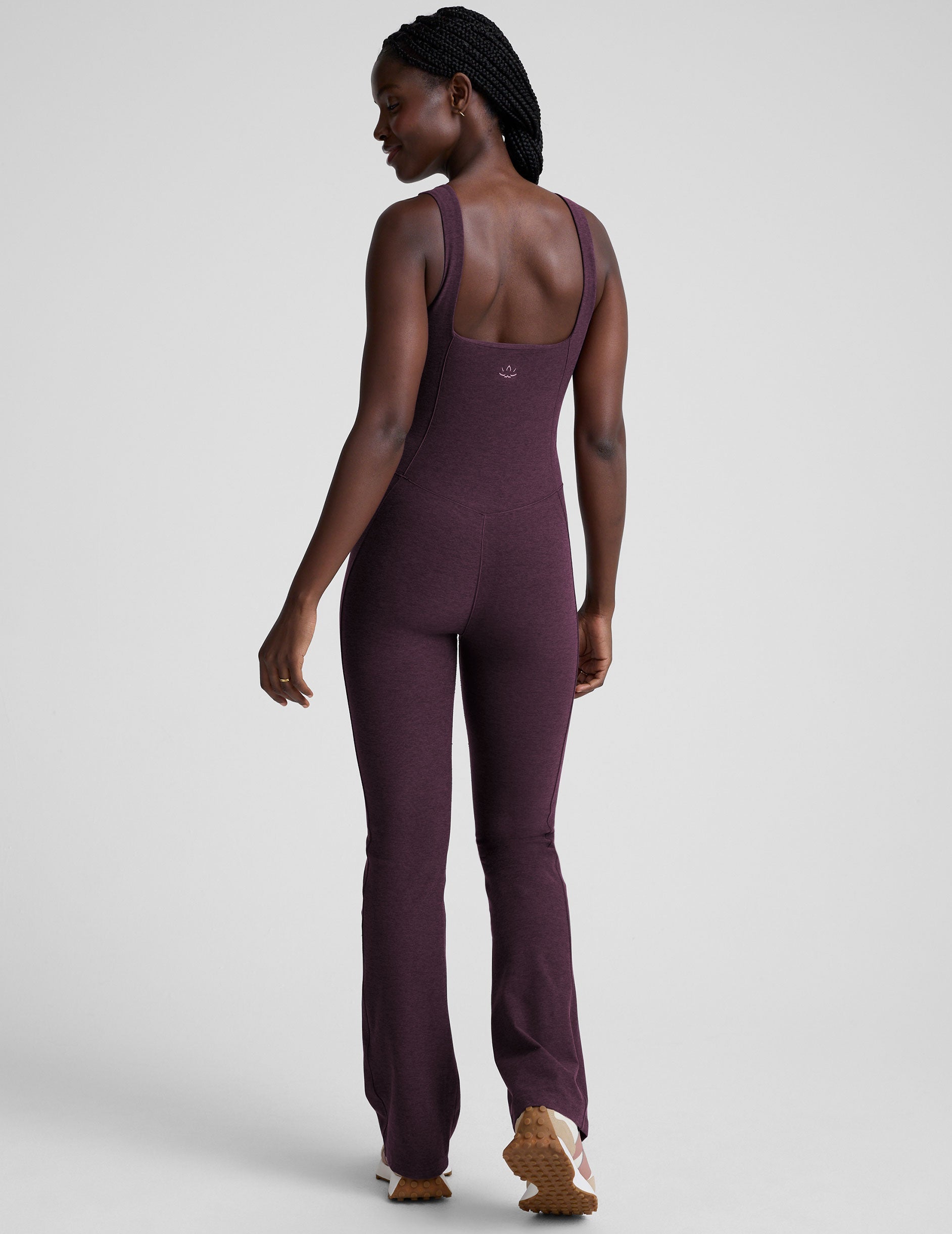 model wearing a purple square neck bootcut sleeveless jumpsuit on a plain background.