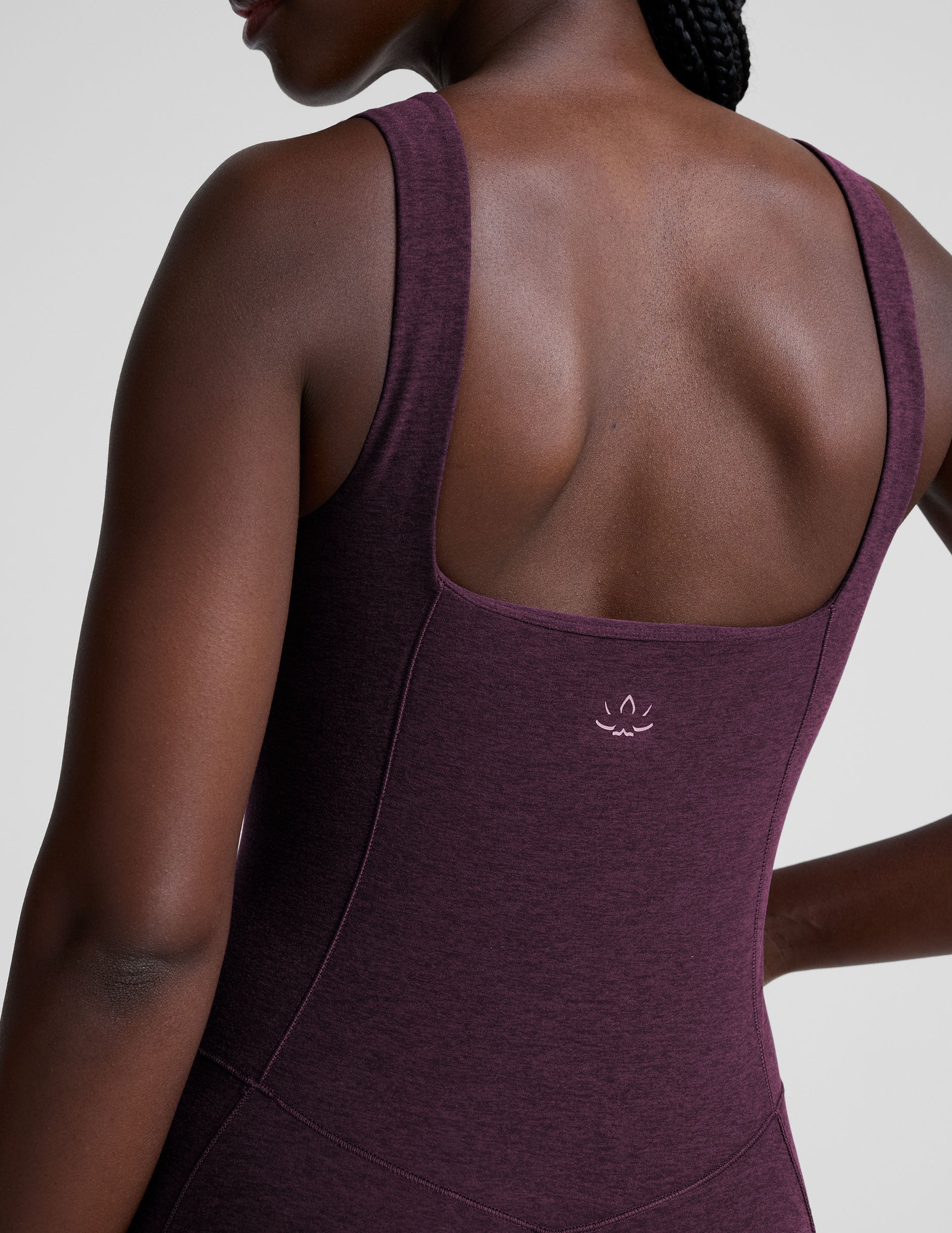 model wearing a purple square neck bootcut sleeveless jumpsuit on a plain background.