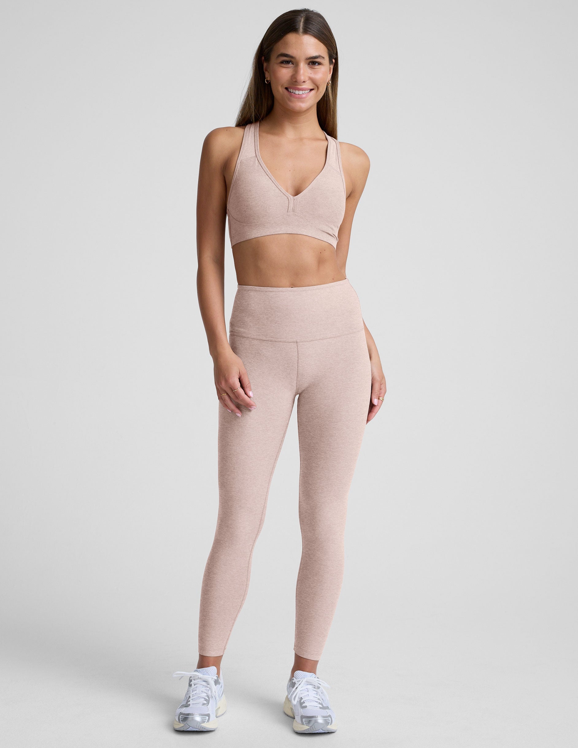 model wearing a pink v-neck sports bra and leggings on a plain background.