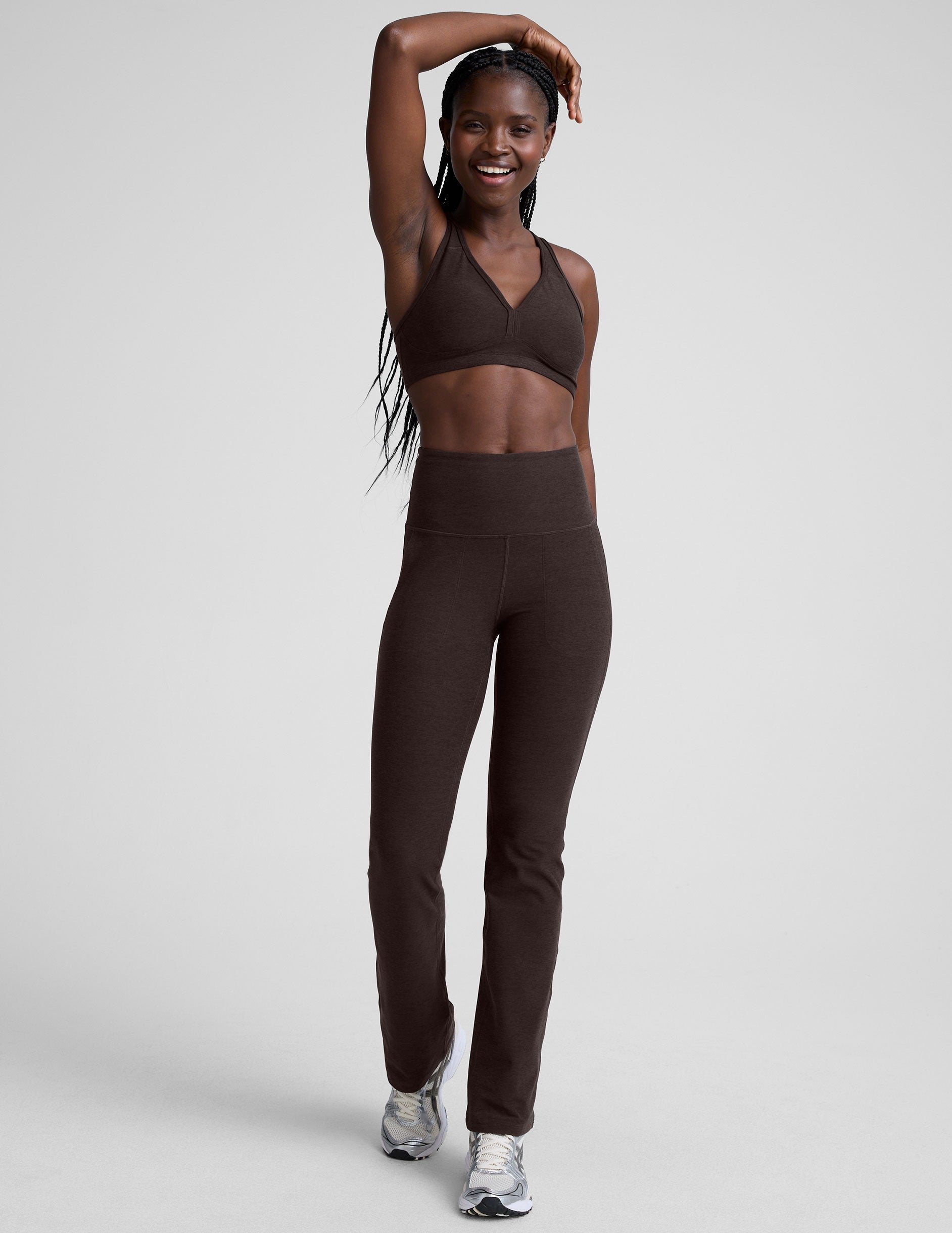 woman wearing a brown v-neck sports bra and pants on a plain background.